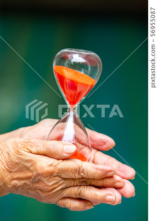 Senior woman's hands holding red hourglass in blue swimming pool background, Close up & Macro shot, Selective focus, Time concept Senior woman's hands holding red hourglass in blue swimming pool background, Close up & Macro shot, Selective focus, Time concept 56955087