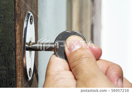 Woman's left hand use a key for lock or unlock wooden door, Close up & Macro shot, Selective focus, Security concept 56957238
