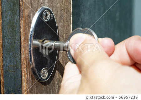 Woman's left hand use a key for lock or unlock wooden door, Close up & Macro shot, Selective focus, Security concept 56957239