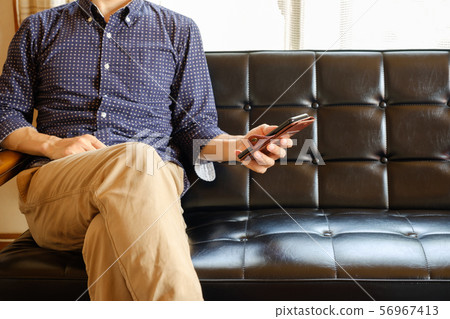 A man who operates a smartphone on his sofa at home A man who operates a smartphone on his sofa at home 56967413