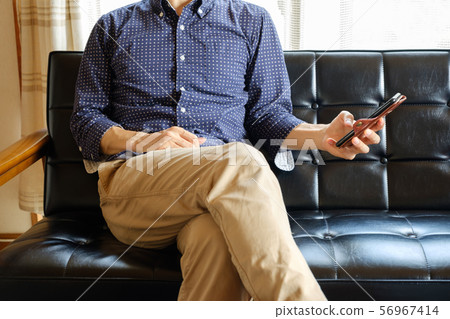 A man who operates a smartphone on his sofa at home A man who operates a smartphone on his sofa at home 56967414