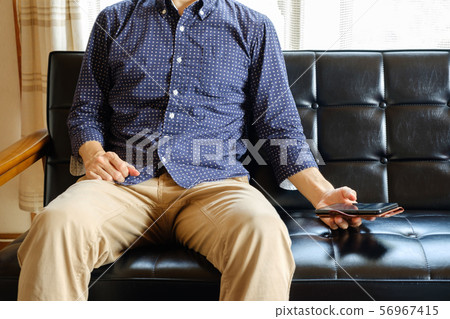 A man who operates a smartphone on his sofa at home A man who operates a smartphone on his sofa at home 56967415