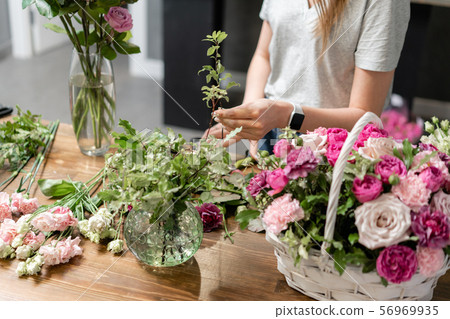 Woman florist create flower arrangement in a wicker basket. Beautiful bouquet of mixed flowers 56969935