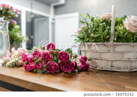 Woman florist create flower arrangement in a wicker basket. Beautiful bouquet of mixed flowers Woman florist create flower arrangement in a wicker basket. Beautiful bouquet of mixed flowers 56970142