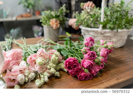 Woman florist create flower arrangement in a wicker basket. Beautiful bouquet of mixed flowers 56970332