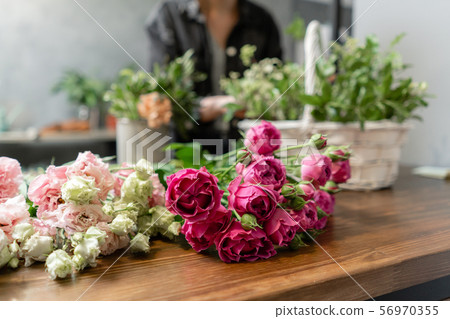 Woman florist create flower arrangement in a wicker basket. Beautiful bouquet of mixed flowers 56970355