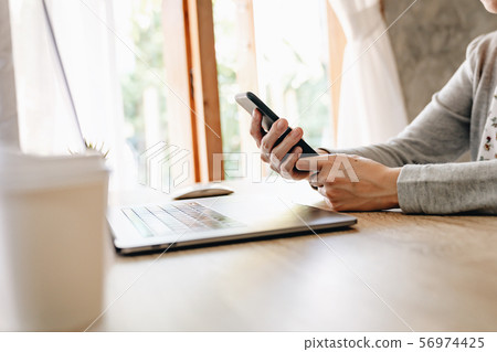 Asian woman holding phone and using computer Asian woman holding phone and using computer 56974425