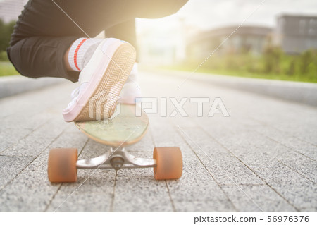 Image of woman's legs in white sneakers riding skateboard on street in city on summer day. 56976376