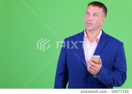 Mature macho businessman in suit thinking while using phone 56977100