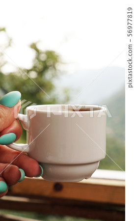 Hand white cup of hot coffee. In the morning, cold mountain views 56977819