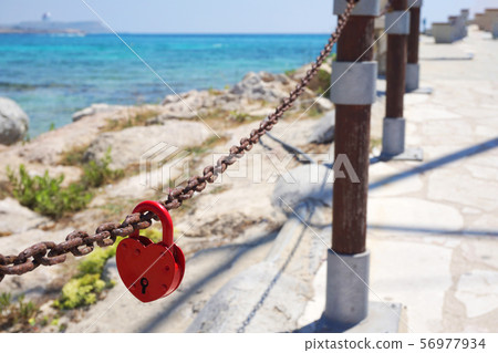 Red love padlock attached to chain. Rusty lock with heart shape carved hanging outdoors. Valentines Red love padlock attached to chain. Rusty lock with heart shape carved hanging outdoors. Valentines 56977934