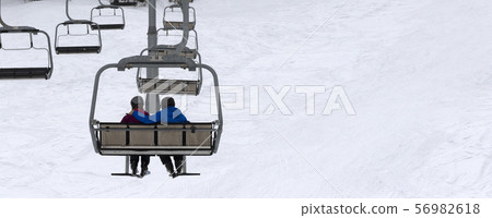 Two skiers on chair-lift in gray day Two skiers on chair-lift in gray day 56982618