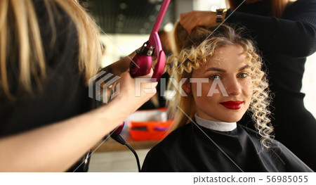 Young Woman Getting Curly Hair by Curling Iron Young Woman Getting Curly Hair by Curling Iron 56985055