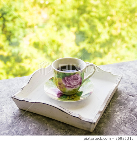 Hot morning coffee in small floral design cup on shabby chic vintage white tray on window sill in Hot morning coffee in small floral design cup on shabby chic vintage white tray on window sill in 56985313