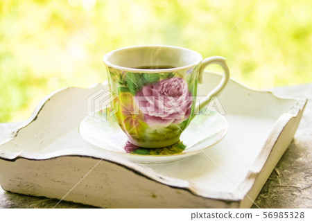 Hot morning coffee in small floral design cup on shabby chic vintage white tray on window sill in 56985328