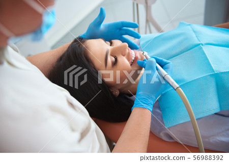Male dentist in protective mask doing teeth cleaning for pretty lady 56988392
