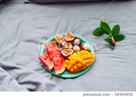 Plate with tropical fruit and flower in grey bed, 56994950