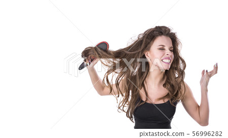 cute girl pulls out a comb from tangled hair and screams into the camera on a white background. Hair 56996282