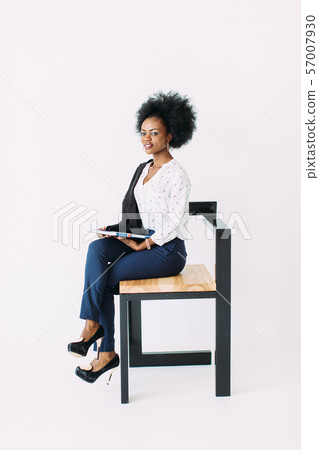 Cheerful young afro american business woman talking on cell phone, sitting on the chair, isolated on white background in studio Cheerful young afro american business woman talking on cell phone, sitting on the chair, isolated on white background in studio 57007930