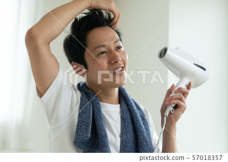 Young Japanese man drying her hair with a dryer Young Japanese man drying her hair with a dryer 57018357