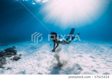 Freediver girl with fins dive over sandy sea in ocean. 57025818