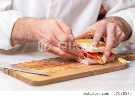 Chef finalizes the sandwich with ham and salad on the wooden board. Chef finalizes the sandwich with ham and salad on the wooden board. 57028573