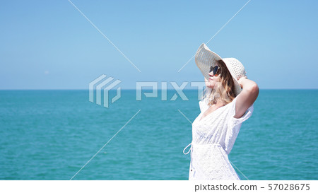 Young woman standing on sand near sea and holding a hat 57028675