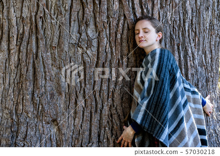 Young woman leaning against the trunk of a large 57030218
