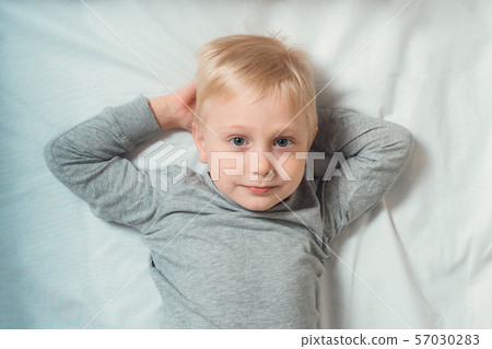 Blond cute boy lies hands behind his head. White 57030283