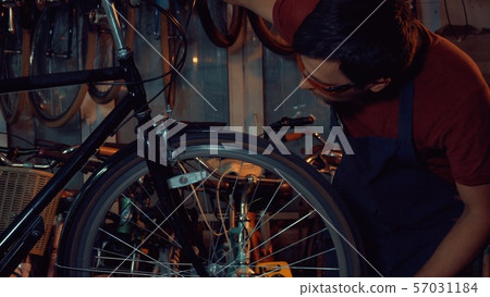 theme small business bike repair. Young brunette Caucasian man in protective glasses, gloves and theme small business bike repair. Young brunette Caucasian man in protective glasses, gloves and 57031184