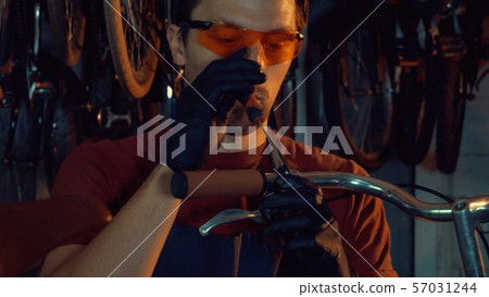 theme small business bike repair. A young Caucasian brunette man wearing safety goggles, gloves and theme small business bike repair. A young Caucasian brunette man wearing safety goggles, gloves and 57031244