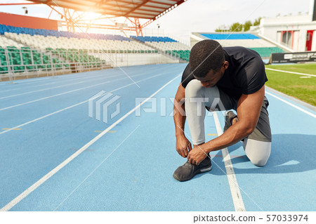 Sportsman ties his trainers, sitting on the running track, preparing 57033974