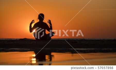 Young woman sits by the sea in lotus position at sunset, meditates 57037898