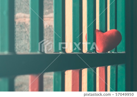 A little red heart pillow on a green steel fence. 57049950