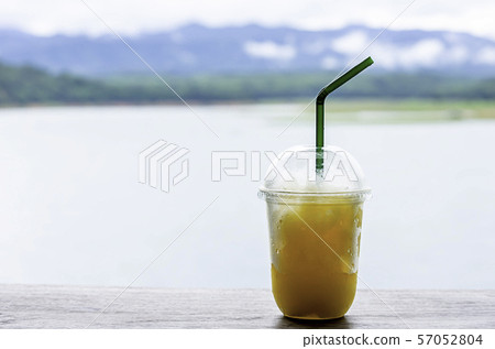 Glass of cold Orange juice smoothie on the table Background blurry views sky water and mountain. 57052804
