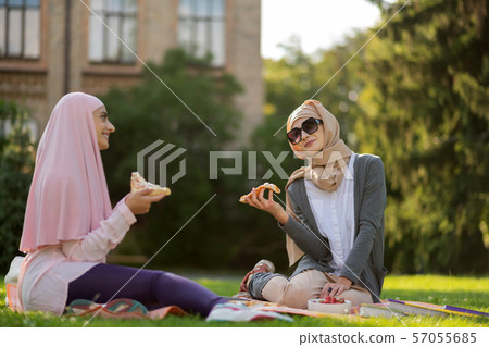 Muslim woman in sunglasses eating pizza with friend outside 57055685