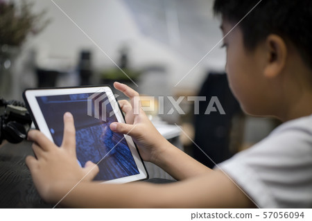 Asian little boy playing game on digital tablet at home Asian little boy playing game on digital tablet at home 57056094