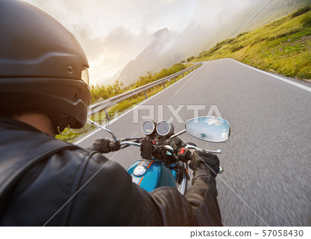 Motorcycle driver riding in Alpine highway, handlebars view, Dolomites, Europe. Motorcycle driver riding in Alpine highway, handlebars view, Dolomites, Europe. 57058430
