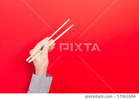 Male hand with chopsticks on red background. Male hand with chopsticks on red background. 57061694