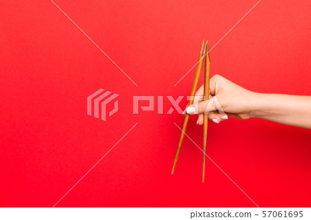 Wooden chopsticks holded with female hands on red Wooden chopsticks holded with female hands on red 57061695