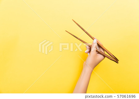 Female hand with chopsticks on yellow background. Female hand with chopsticks on yellow background. 57061696