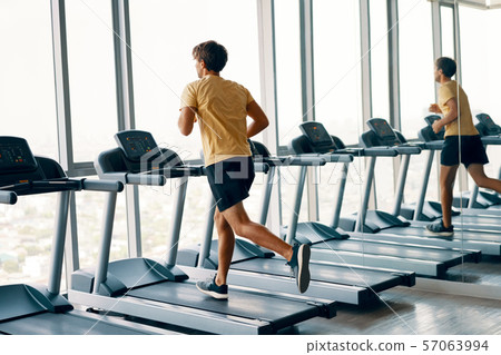 Full length portrait of young sports man running on a treadmill at gym 57063994
