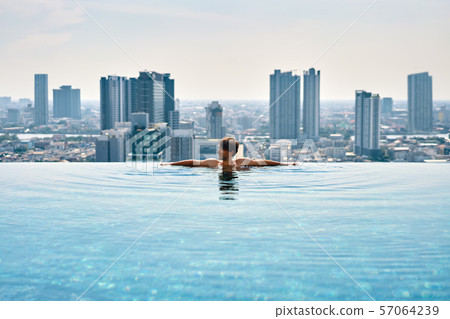 Young man relax on the edge of swimming pool in roof top of hotel Young man relax on the edge of swimming pool in roof top of hotel 57064239