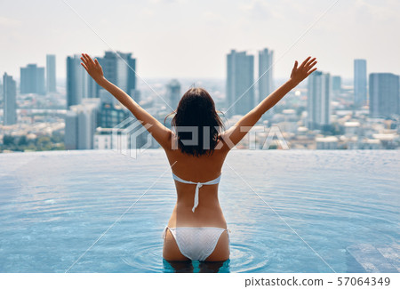 Back view of happy freedom woman with raised arms enjoy her summer vacation on swimming pool 57064349