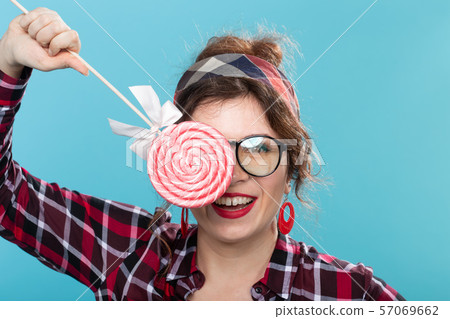 candy, fashion and fun concept - pin-up woman closed her eye by lollipop on blue background candy, fashion and fun concept - pin-up woman closed her eye by lollipop on blue background 57069662