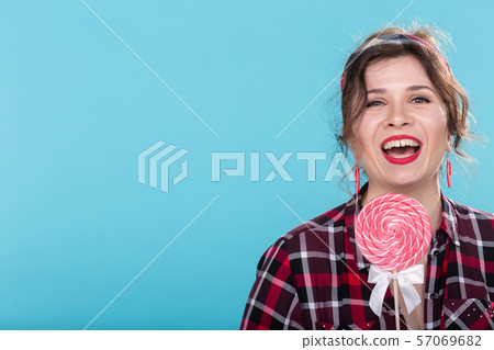 fashion, yammy and candy concept - laughing woman with lollipop in pin-up style on blue background 57069682