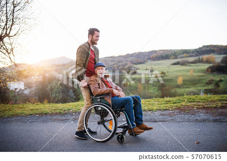 Young man and his senior father in wheelchair on a walk in town. 57070615