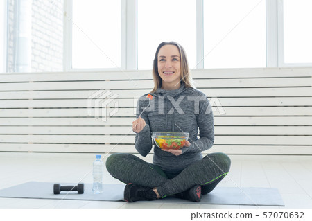 Sport, healthy lifestyle and people concept - young woman with salad and a dumbbell sitting on the Sport, healthy lifestyle and people concept - young woman with salad and a dumbbell sitting on the 57070632