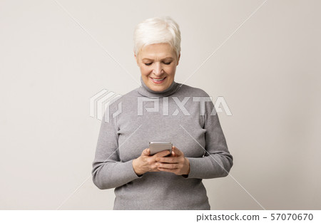 Elderly lady using smartphone over light studio background Elderly lady using smartphone over light studio background 57070670