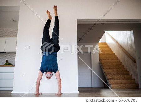 A senior man indoors at home, doing handstand exercise indoors. 57070705